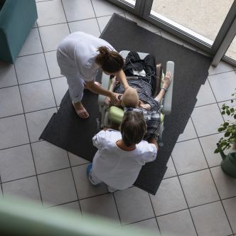 Deux infirmères affairées auprès d'une personne en fauteuil, vu du dessus. Crédit photo : David Cesbron